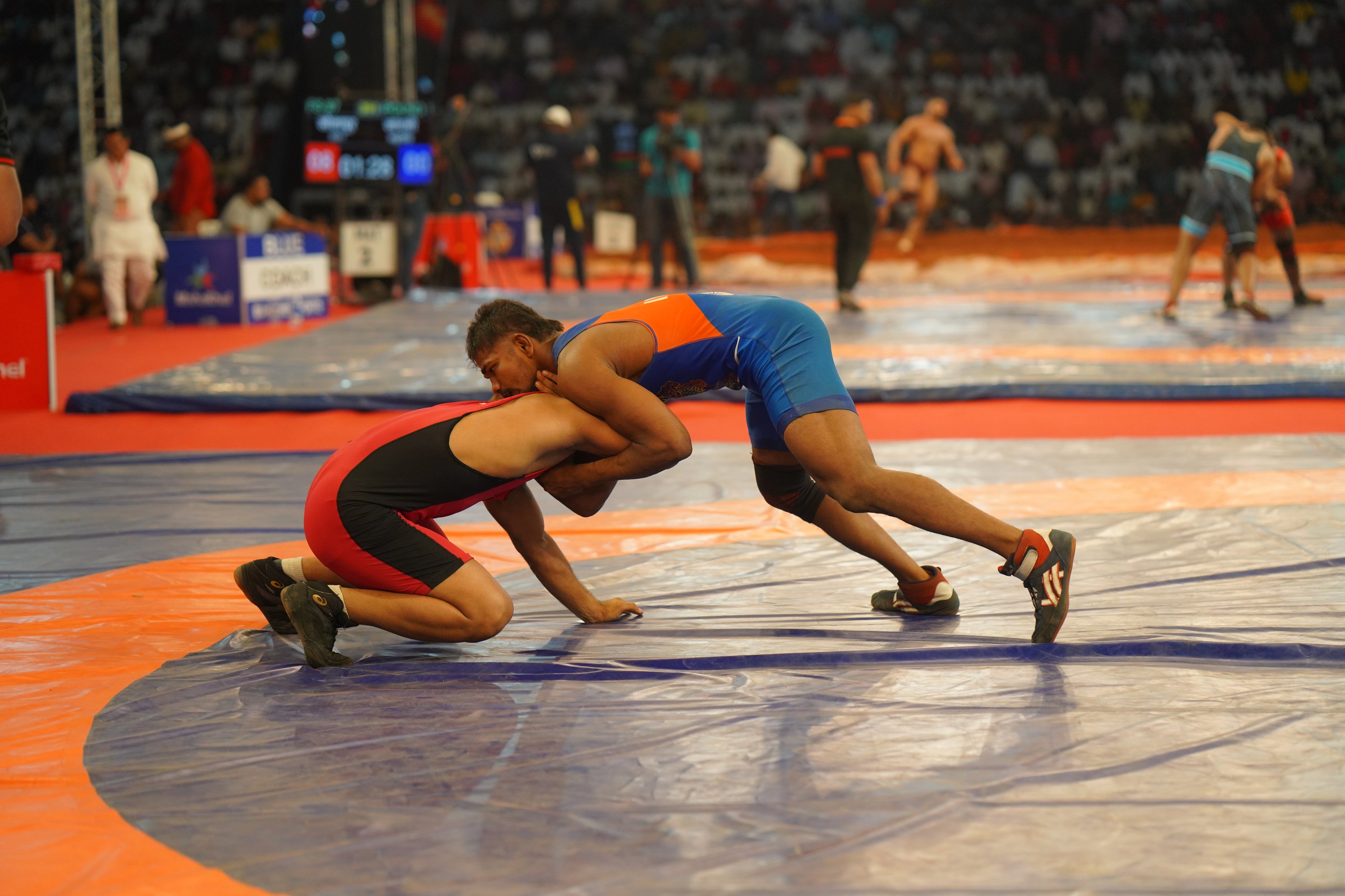 Wrestlers grappling intensely on mat with coaches watching at Maharashtra Kesari arena with sponsor banners
